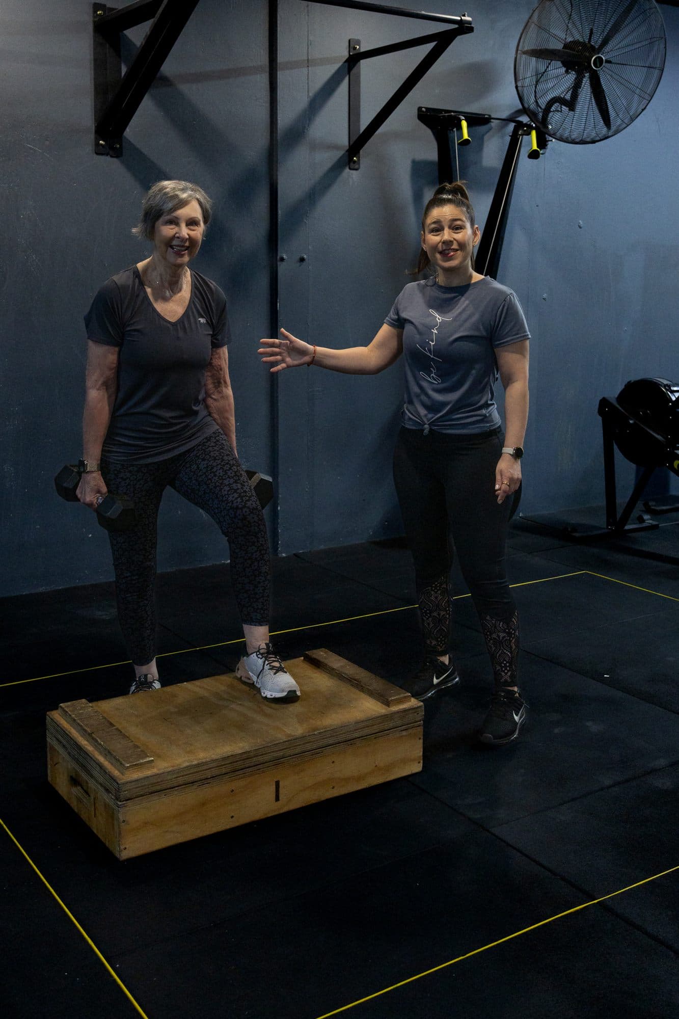 A client stepping onto a box holding dumbbells while Alex coaches beside her