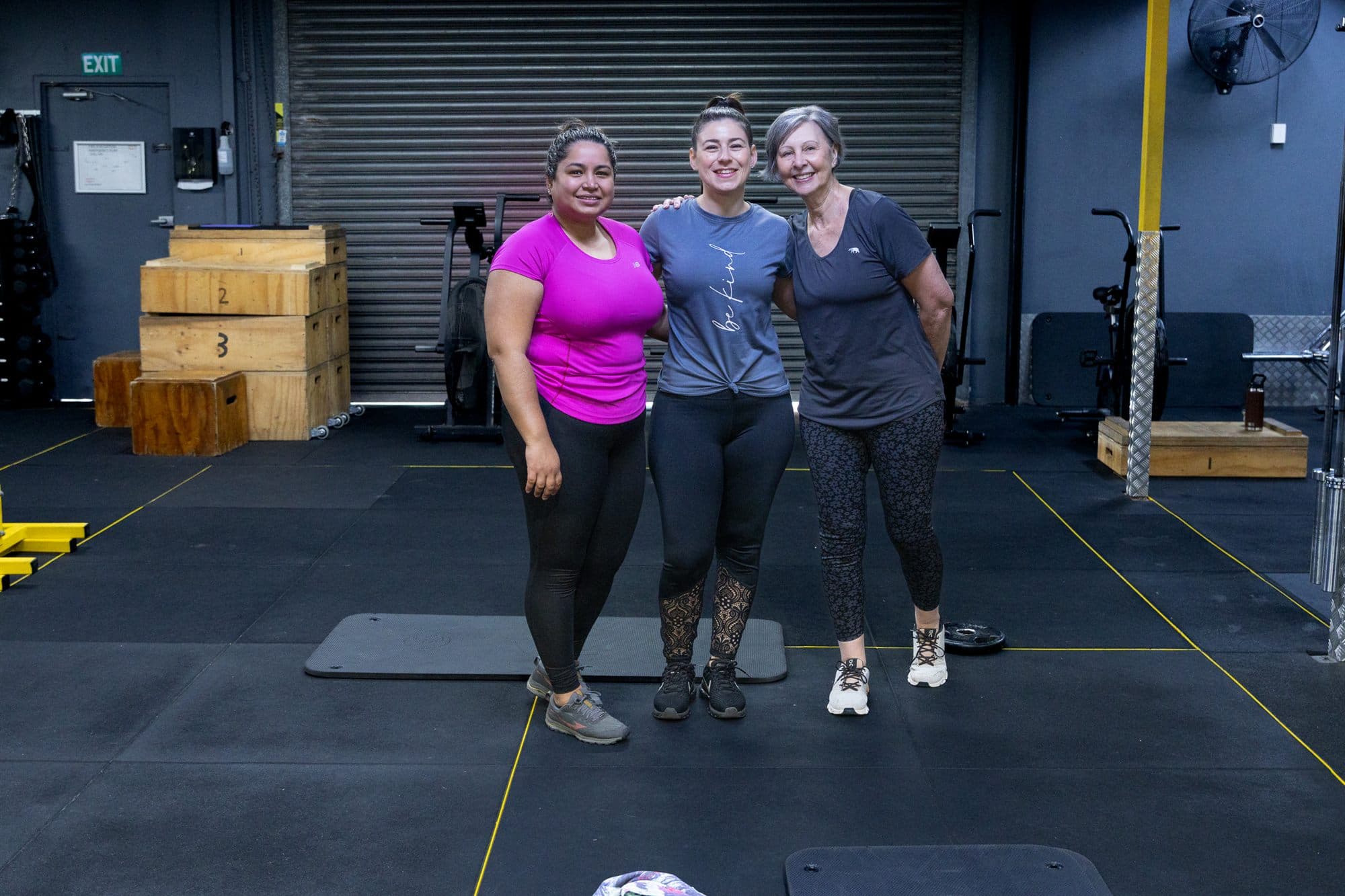 Alex standing arm in arm with two clients on the gym floor, all three smiling