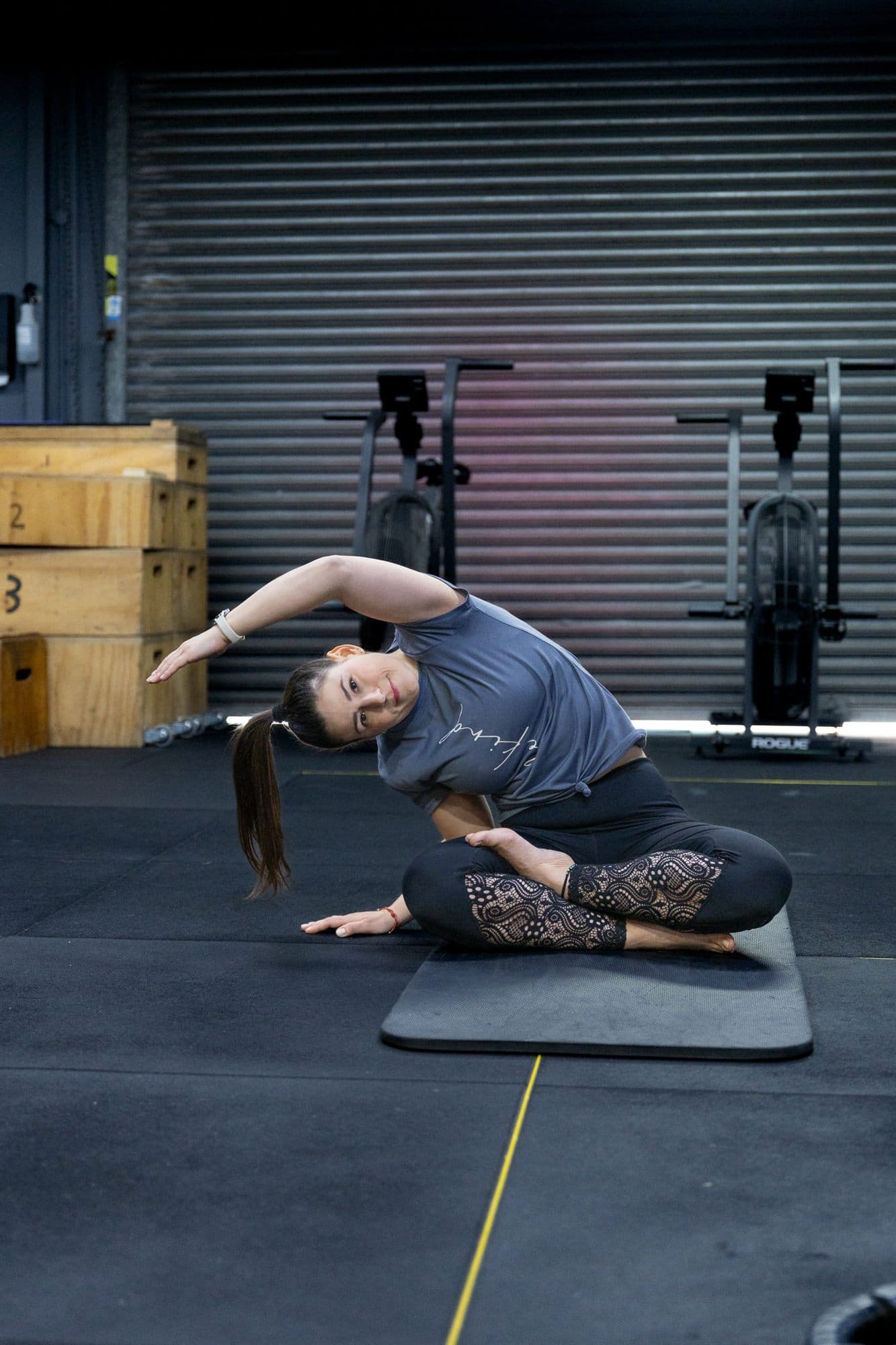 Alex seated on a mat, reaching overhead through a long side bend to open one side of her ribs