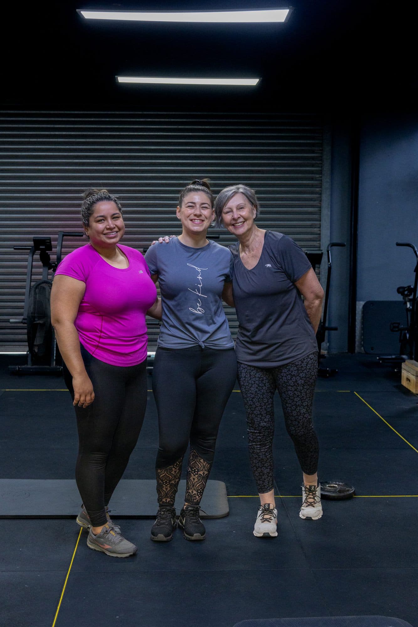 Alex standing arm in arm with two clients on the gym floor, all smiling