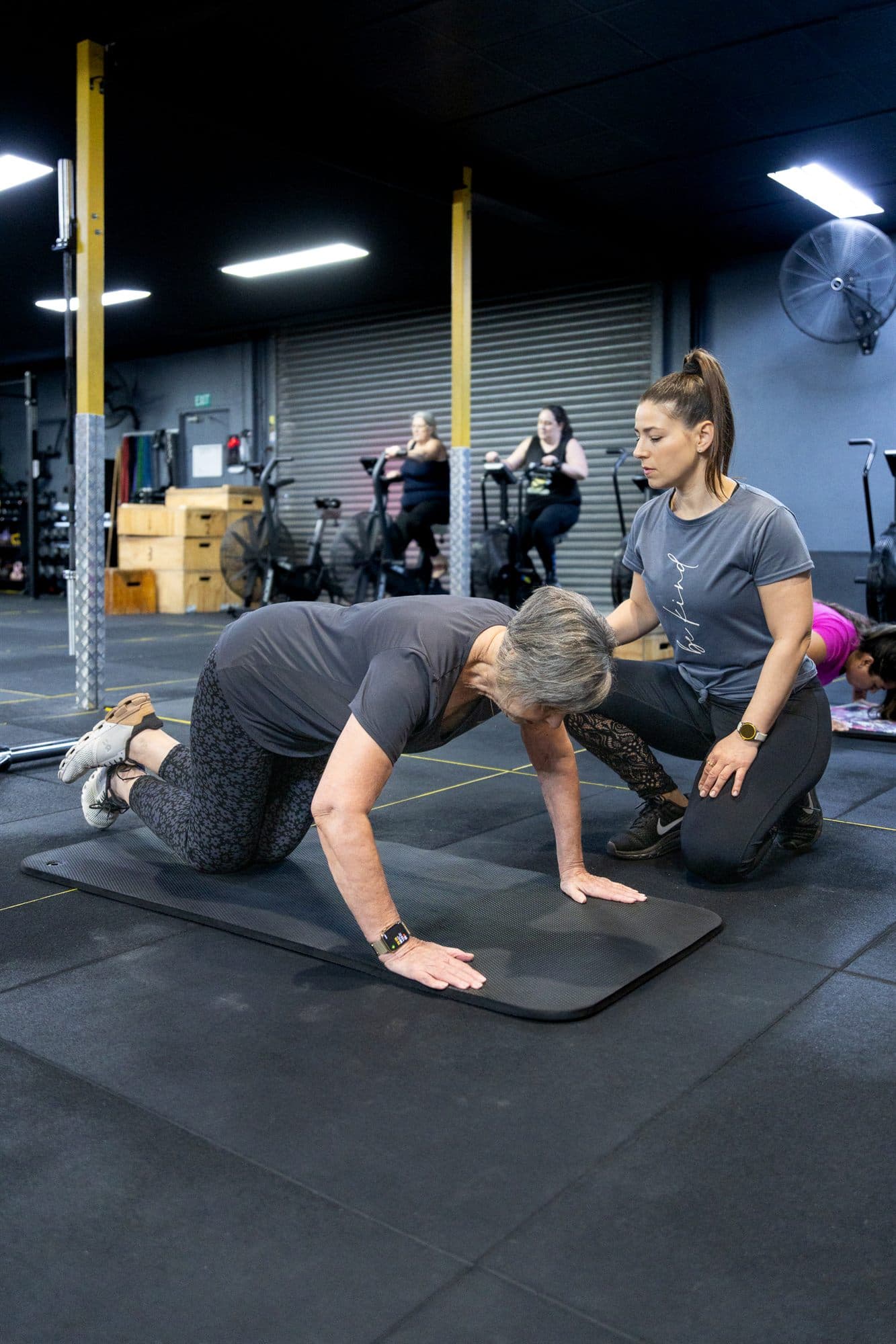 Alex kneeling on a mat, coaching a client through a stretch on all fours