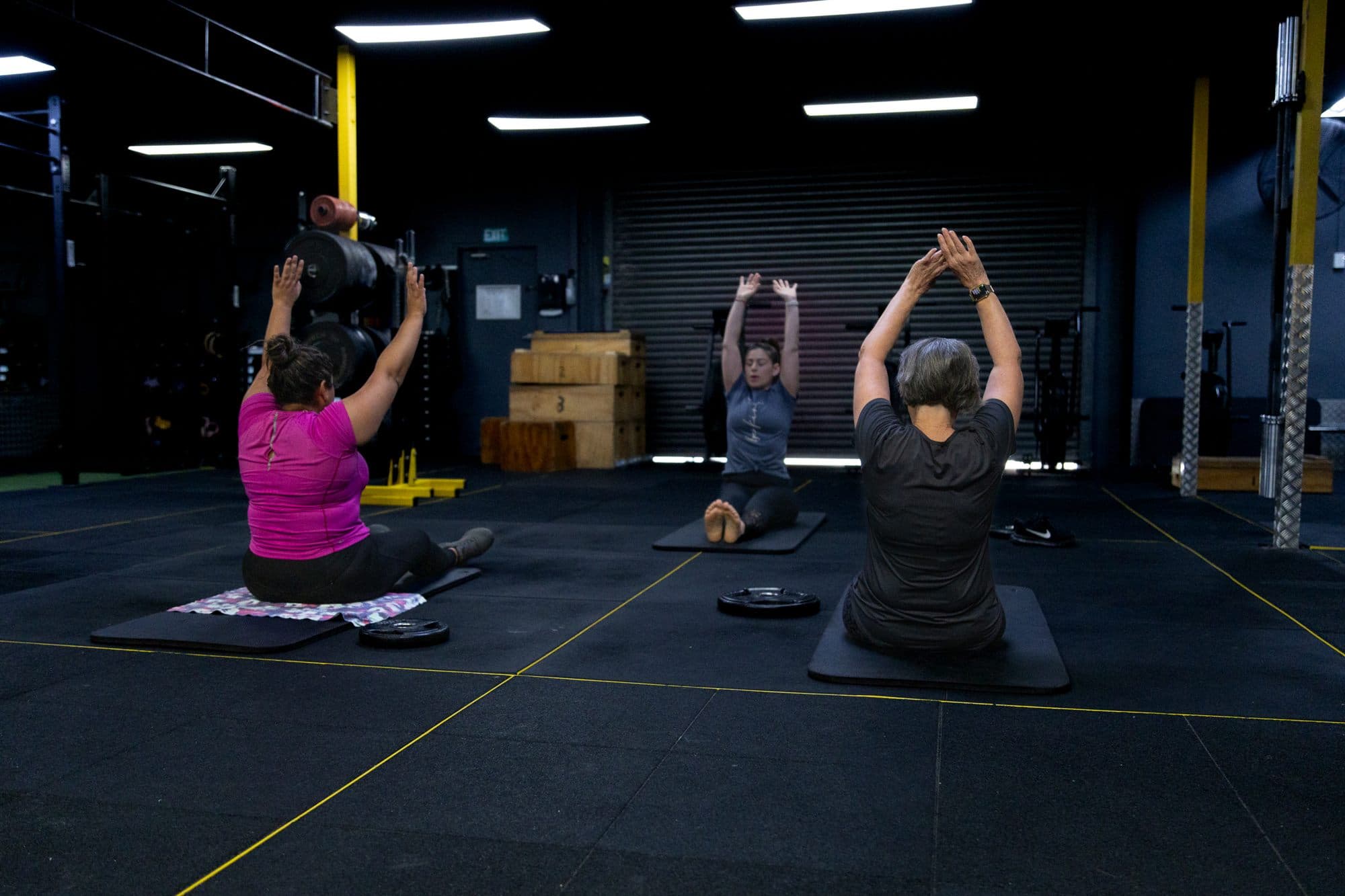 Three women seated on mats, reaching both arms overhead together